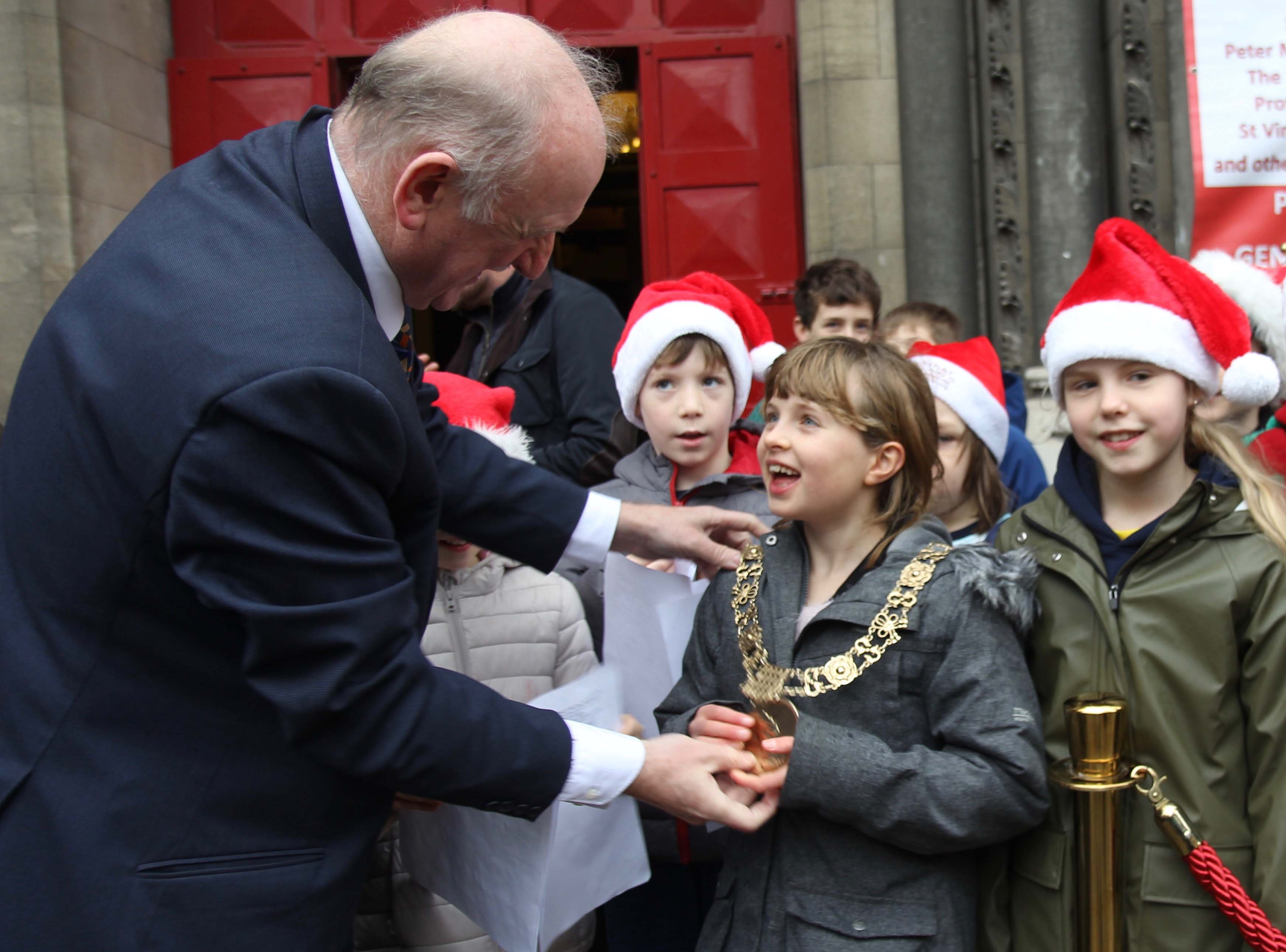 A young member of the Choir of Kildare Place School tries on the Lord Mayor Nial Ring's chain of office at the launch of the Black Santa Sit Out 2018.