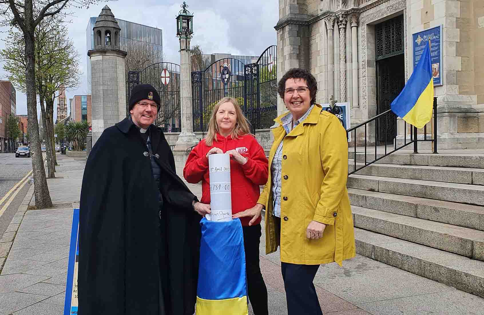Dean Stephen Forde has presented a cheque for £56,784 to Rosamond Bennett, Chief Executive of Christian Aid Ireland, and Jenny Williams, Chief Executive of Habitat for Humanity Ireland, raised through Belfast Cathedral's special Black Santa Sit-out for Ukraine.